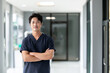 © NaphakStudio - Standing confidently in a bright medical facility, a male doctor surgeon in dark blue scrubs crosses his arms, his serious demeanor and professional attire indicating his readiness for surgery.