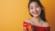 © siripimon2525 - Close-up of a Japanese teenage girl smiling and holding a gift box, wearing a cute red top, standing in front of a yellow background, Portrait close-up, hyper-realistic, high detail, photorealistic,