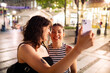© Marko Geber - Lesbian couple laughing while using smartphone in city