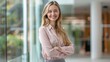© cvetikmart - Young European business woman in formal attire, arms crossed, smiling, standing in front of a glass conference room, long blonde hair, wearing a pink blouse. European business woman arms crossed