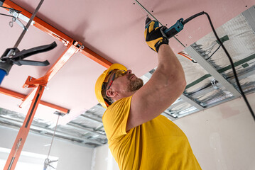 Wall Mural - The worker screwing plasterboard to the ceiling. He is using special electric screwdriver. A red plasterboard improve the fire resistance of ceiling structures.