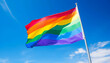 © Gun - Bright and Vibrant Rainbow Flag Waving Proudly Against a Clear Blue Sky with Fluffy White Clouds