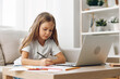 © SHOTPRIME STUDIO - Young girl focused on online learning, sitting at a table with a laptop and pen, studying diligently