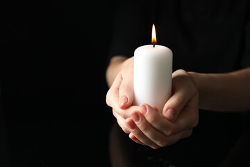 Wall Mural - Woman holding burning candle on black background, closeup. Space for text