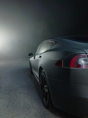 Sleek black car on a foggy night with a bright light in the background