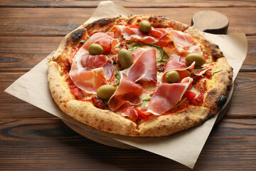 Wall Mural - Tasty pizza with cured ham, olives and sun-dried tomato on wooden table