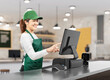 © phonlamaiphoto - Active asian seller wear green uniform smiling with point of sale terminal or cashier desk