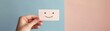 © TENTIP - A hand holding a small card with a smiley face in front of a split color background featuring blue and peach tones, symbolizing positivity.