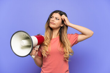 Wall Mural - Young Russian girl isolated on blue background holding a megaphone and having doubts