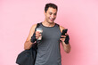 © luismolinero - Young sport caucasian man with sport bag isolated on pink background holding coffee to take away and a mobile