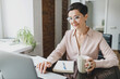 © shurkin_son - Mature smiling elegant confident business lady or female lawyer in stylish eyeglasses working on laptop sitting in office chair at table with coffee cup, checking e-mail or having break