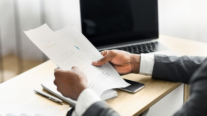 Leinwandbilder - A businessman sits at a desk, carefully reviewing a document with graphs and charts.