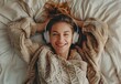 © MYDAYcontent - A woman lies in bed with a white blanket, wearing headphones and smiling.