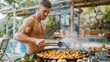 © Yotsaran - Shirtless bodybuilder cooking at barbecue, showcasing muscular back, healthy sides on table