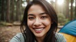 © Tom - A young asian woman with long dark hair and a radiant smile, standing in a forest clearing with a tent in the background, enjoying the natural surroundings.