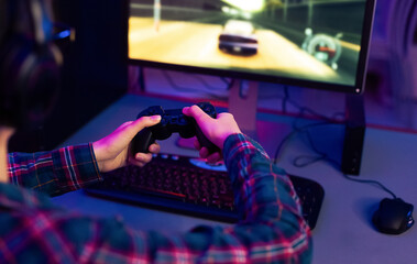 Aufkleber - This image shows a gamer playing a racing video game at their computer desk. The gamer is wearing a plaid shirt and using a black video game controller. The computer monitor is displaying racing game
