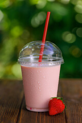 Wall Mural - strawberry milkshake or smoothie in disposable plastic glass with straw on table outdoors