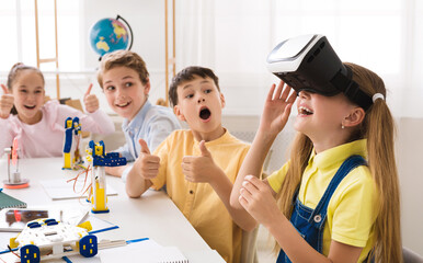 Poster - A group of elementary school students are engaged in a STEM class, with one student wearing a VR headset and experiencing a virtual world. The other students are looking on with excitement