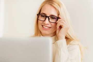 Aufkleber - A blonde woman wearing glasses smiles while using a laptop computer.