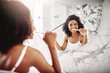© peopleimages.com - Happy, woman and reflection with brushing teeth in bathroom for dental care, cleaning and grooming. Home, person and toothbrush with hair check in mirror for oral hygiene, routine and fresh breath
