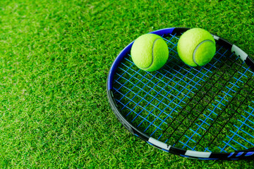 Tennis Gear on Green Grass Surface. Tennis racket and two balls arranged on green grass. Overhead shot, with empty space for text, suitable for banners.