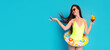 © Prostock-studio - A young woman in a yellow swimsuit holds a colorful cocktail and an inflatable ring while smiling against a bright blue background, copy space