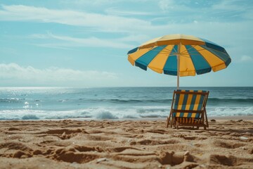 Poster - A sunny and peaceful beach scene featuring a yellow and blue striped umbrella alongside a matching lounge chair, set on the sandy shore with calm waves in the background.