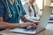 © Aleena - Nurse and doctor working on laptop in hospital office, white male nurse wearing uniform with stethoscope standing near desk talking to female student while using computer for medical research
