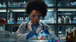 © HumanArtPixels - Pharmaceutical lab specialist examines medicine vials, hospital patient samples. An African American female medical student conducts research, science laboratory, wearing protective.