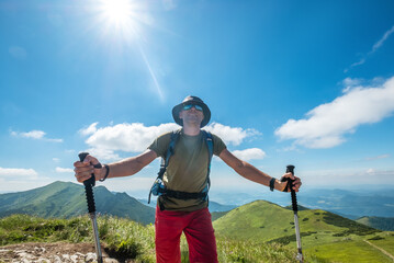 Wall Mural - hiker with trekking poles, backpack navigates rocky mountain trail on sunny day scenic background fe