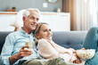 © Penn/peopleimages.com - Watching tv, house and mature couple with movie date, series and film streaming with love and support. News, smile and bonding of happy people together on a living room sofa with food, drink and hug