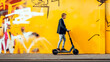 © Garnar - Young man in smart attire rides an electric scooter by a graffiti-covered bright yellow wall, symbolizing vibrant urban youth culture and mobility. Concept of modern lifestyle. Banner. Copy space