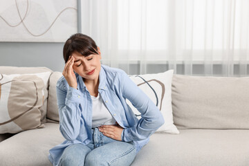 Canvas Print - Upset woman suffering from headache on sofa at home