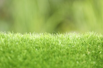 Wall Mural - Green artificial grass against blurred background, closeup