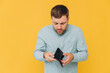 © anatoliycherkas - I'm Broke. Portrait of sad unshaven male bankrupt showing his empty wallet looking at camera. Upset man standing isolated over yellow studio background. Poverty Concept. Lack of money