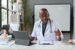 © crizzystudio - African American male doctor working in clinic at desk using laptop in medical coat and stethoscope. organ specialist The patient's anatomy, treatment methods, medical treatments.