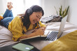 © Daniel - Happy asian female college student writing on notebook at home bedroom lying on bed. Chinise girl studying with laptop
