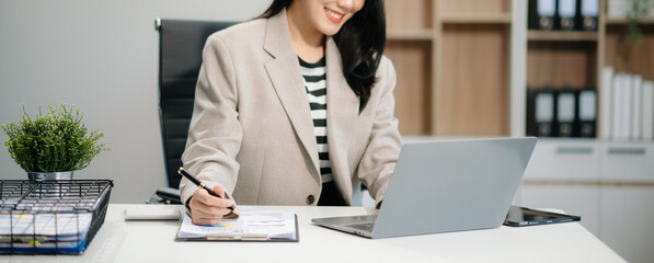 Wall Mural -  Beautiful Asian businesswoman typing laptop and tablet Placed at the table at the office