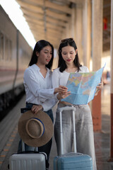 Smiling women on the station platform with happily looking into a smartphone, girls standing at train station take selfie photo on smartphone.