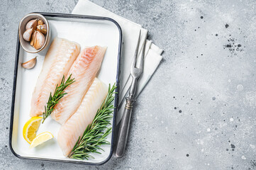 Wall Mural - Uncooked Raw cod loin fillet steaks with herbs in kitchen tray. Gray background. Top view. Copy space