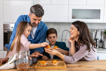 Wall Mural - In the cozy kitchen, a family gathers around the table. With smiles on their faces enjoying the simple pleasures of togetherness and sweetness in every bite.