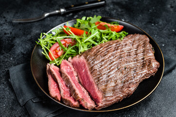 Wall Mural - Grilled medium rare flank beef steak with salad in a plate. Black background. Top view