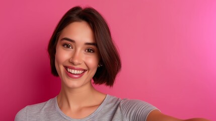 Wall Mural - A woman with short hair is smiling and posing for a picture. She is wearing a gray shirt and has a pink background