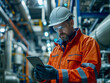 © Deea Journey  - Worker in orange uniform with a hard hat, in a storage room looking at a tablet. Occupational Health and Safety worker in a bright orange Personal protective equipment