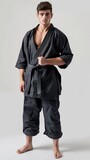 A young man in a black martial arts uniform stands with a focused expression