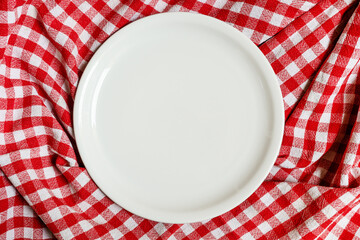 Empty white plate on checkered plaid red and white tablecloth from above as background