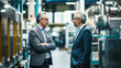 © OMD - Two senior businessmen engaged in a discussion in a modern industrial manufacturing plant, surrounded by machinery and equipment.