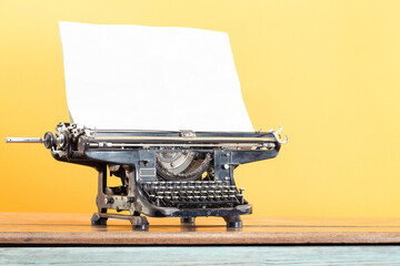 Antique typewriter with sheet of paper blank on retro oak table front yellow background. Vintage old style filtered photo