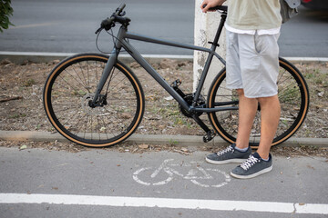 A person stands beside their bicycle on a bike path, with a white line separating the path from the sidewalk. environmentally friendly transport concept