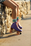 A young woman sits on a stone wall with her roller skates on, enjoying the Miami sunset.